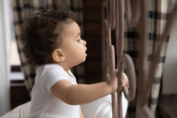 Wall Mural - cute little african american girl toddler child stand holding bed frame look in distance feel curiou