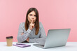 © khosrork - Be quiet. Serious brunette woman in striped shirt sitting at workplace showing silence sign, looking at camera with finger on lips, asking to be silence. Indoor studio shot isolated on pink background
