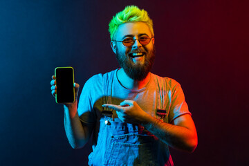 Wall Mural - happy positive bearded hipster man with green hair showing smart phone with blank screen, looking at
