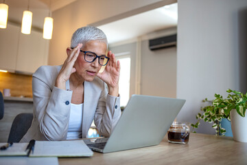 Fototapete - Woman struggling with new technology. Exhausted businesswoman having a headache in modern office. Mature creative woman working at office desk with spectacles on head feeling tired.