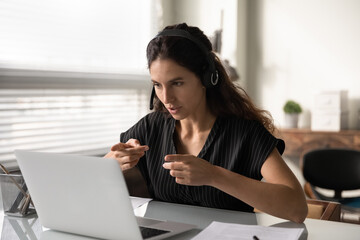 Wall Mural - Distant consultation. Concentrated latin female in headset sit by pc support client remotely assist to solve technical problem. Focused young lady interpreter working online translating simultaneously