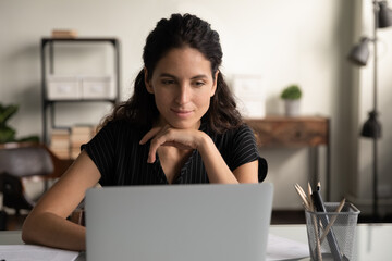 Good work. Smiling positive young lady office worker doing interesting job online reading pleasant email on laptop screen. Happy millennial latin woman sit by laptop at workplace enjoy working process