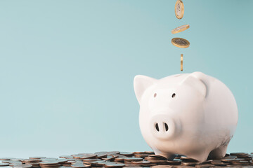 Coins falling and dropping to white piggy bank saving on top of heap of coins and blue background ,money saving for investment and retirement in the future concept.