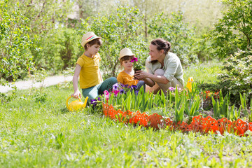 mother and two kids plant flowers in the garden near the houme on spring day. children help mom work in the garden. slow life. enjoy the little things. 