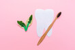 A bamboo toothbrush with green leafs and cut out tooth of felt. Pink background. Flat lay. Copy space. The concept of eco friendly hygiene products