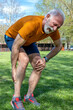 Senior athlete man frowning with muscle pain during training outdoors. Calf leg cramps trauma. Vertical orientation.