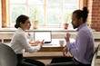 © fizkes - Side view diverse colleagues working on project together, Indian businesswoman and African American businessman discussing strategy, sitting at desk with laptop with white empty screen mockup