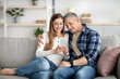 © Prostock-studio - Happy mature couple using smartphone while relaxing on sofa at home