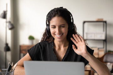 Wall Mural - Welcoming audience. Smiling polite latin female student wear headset attend virtual lecture in conference mode wave greet tutor friends. Positive young woman communicating by video call showing hello