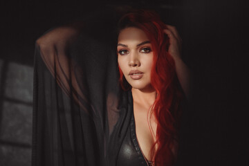 sensual girl with red hair in transparent black clothes looks into the camera.