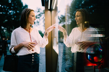 Side view of Caucasian tourist checking schedule on navigation panel tapping sensory for online ticketing, female touching screen for self consulting at electronic system using advanced technology