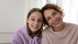 © fizkes - Head shot portrait of smiling affectionate young teenager kid girl posing at home with caring mother. Happy sincere bonding mommy looking at camera with cute little adolescent child daughter.