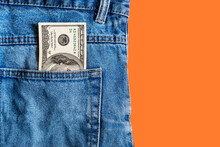 Money In Pocket. One Hundred American Dollars Bill In A Jeans Pocket On A Orange Background. Copy Space. Concept Of Earning And Saving Money.
