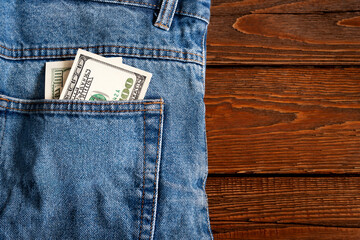 Money in pocket. One hundred dollar bill in a denim jeans pocket on a wooden background. Copy space. Concept of earning and saving money.