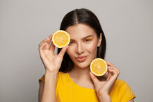 Portrait Of Attractive Young Healthy Model Woman With Clear Skin And Straight Brown Hair Holding Lemon Fruits On White Background. Diet, Skincare And Facial Treatment Concept