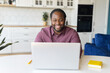 © Vadim Pastuh - Cheerful African-American freelancer is using laptop for work on the distance, black guy sitting at the desk and typing, looks at the screen and laughs, enjoying remote work and free work schedule