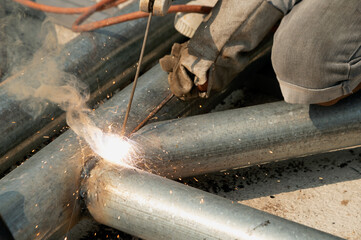 Wall Mural - A welder is sitting on a steel roof frame and is welding steel pipes and wearing masks and leather gloves.