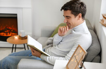 Handsome Man Reading Book Near Fireplace At Home