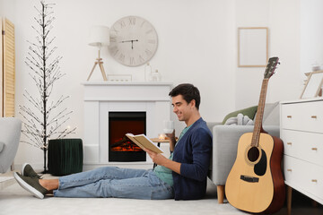 Handsome man reading book near fireplace at home