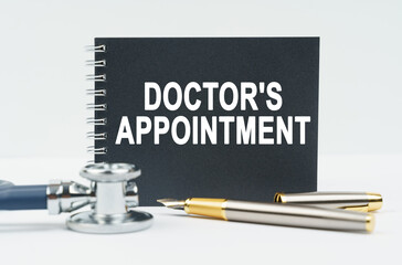 On a white background lies a stethoscope, a pen and a black notebook with the inscription - DOCTORS APPOINTMENT