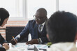 © xartproduction - Mature afroamerican businessman to discuss information with a younger colleague. People working and communicating while sitting at the office desk together with colleagues sitting.