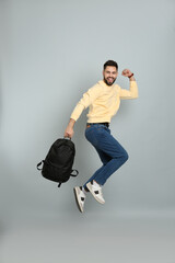Wall Mural - Emotional man with stylish backpack jumping on light grey background