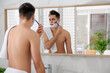 © New Africa - Handsome young man shaving with razor near mirror in bathroom