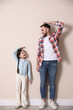 Father and daughter comparing their heights near beige wall indoors