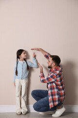 Wall Mural - Father measuring daughter's height near beige wall indoors, space for text