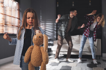 Canvas Print - Little girl punishing toy bunny while her parents fighting on background, space for text. Domestic violence