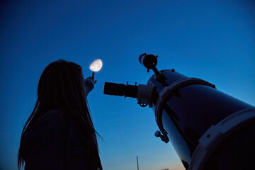 woman looking at night sky with amateur astronomical telescope.