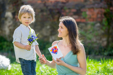 Poster - Beautiful kid and mom in spring park, flower and present. Mother getting gift from toddler boy for Mothers day