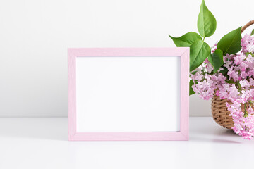 Wall Mural - photo frame and bouquet of lilacs in basket on white table. front view.