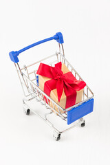 Wall Mural - gift box with a red bow and ribbon in a metal shiny shopping trolley on wheels on a white background. close-up