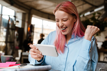 Wall Mural - Young woman with pink hair using cellphone while studying in cafe