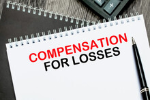 Text COMPENSATION FOR LOSSES To The Background Of A Notebook, Pen. The Concept Of Business And Education.