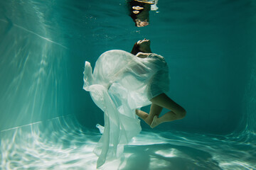 Wall Mural - peaceful young woman in white elegant dress swimming in pool