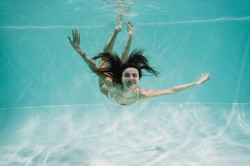 Wall Mural - cheerful young woman in white swimwear swimming in pool