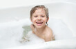 © Olga - the child sits in the bath in the water with foam and laughs, makes a funny expression on his face. concept baby loves to wash