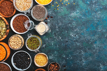 Various organic superfoods, beans, grains, cereals, legumes, seeds in reusable cans and jars. Copy space top view. Blue background