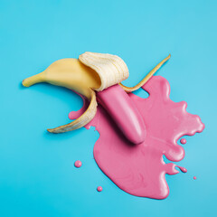 Wall Mural - Peeled banana with pink fluid puddle against vibrant blue background. Minimal summer fruit concept. Vegetarian creative food banner with copy space. Flat lay, top view.