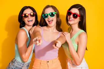 Sticker - Photo of young beautiful excited crazy smiling funky girls in sunglass point finger you isolated on yellow color background