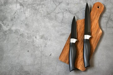 Two black kitchen knifes lies on a wooden cutting board on a gray concrete background. Flat lay, copy space.