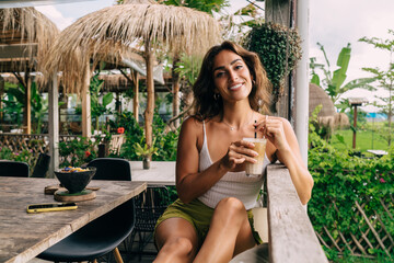 Wall Mural - Cheerful ethnic woman drinking coffee in outdoor cafe