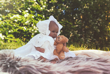  Little ethnic doll in white lacy dress in front of white flowering bush with her little teddy bear