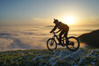 Mountain Biker Riding Downhill Above the Clouds at Sunset.