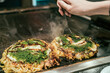 Japanese style pancake okonomiyaki handmade on hot grill plate at restaurant. female hands customer ready to eat okonomiyaki on teppanyaki pan. local food in osaka japan.