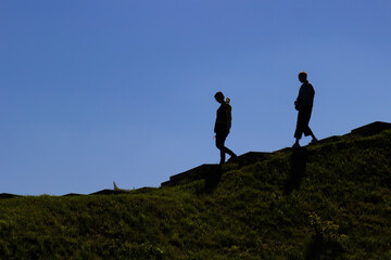 Silhouettes of two people going down the hillside. Dark landscape