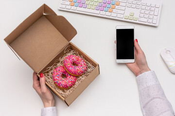 A businesswoman ordered delicious doughnuts for lunch, girl's hands with a box of doughnuts, desk in the office, top view, flat lay