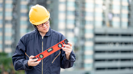 Wall Mural - Asian maintenance worker man holding red aluminium spirit level tool or bubble levels at construction site. Equipment for civil engineering project